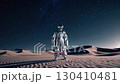 Astronaut in silver suit standing on desert at night under starry sky. Space exploration theme 130410481