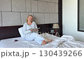woman in tracksuit sitting on bed in hotel opens laptop starts working work online european adult woman at home 130439266
