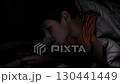 A boy, shielded by a blanket, focuses intently on his phone in the darkness. The scene emphasizes the influence of technology on childhood and its potential effects on sleep and well-being. 130441449