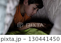 A young boy is focused on his phone while lying under a blanket in the dark. The image captures the quiet moments of gaming but raises awareness of the impact of nighttime device use. 130441450