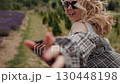 Happy blonde woman wearing sunglasses and casual clothes joyfully runs through lavender field, her hair flowing in wind, extending hand towards the viewer. Blonde woman running. Concept Follow Me 130448198