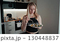 Fit sportswoman consuming nutritious salad, mindfully savoring fresh ingredients while standing in sleek modern kitchen with white cabinets and black countertop. Sportswoman eating healthy green salad 130448837