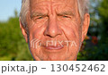 Portrait of old man with gray hair and deep wrinkles on face with slight unshaven face looks at camera. Stands alone in park on summer evening. Look expresses subtle feelings calmness and wisdom 130452462
