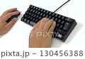 A person uses a mouse with his left hand and types with his right hand on a black keyboard on a white table. 130456388