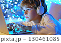 Young male student wearing headphones, working intently on laptop, surrounded by glowing blue bokeh light, capturing digital engagement and focus 130461085