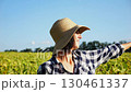Happy smiling female farmer looks into sunflower field and enjoys harvest. Portrait of adult beautiful agronomist in straw hat with yellow plantation at background. Concept of agricultural business 130461337