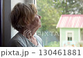 Elderly woman looks thoughtfully out of window, reminiscing about past or longing for other times. The loneliness of the elderly. Isolation during pandemics and viruses. Old people in a nursing home 130461881