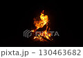 Bright flames flicker and twist in the dark, illuminating the surroundings. The fire crackles softly, providing warmth and a comfortable ambiance for people gathering nearby. 130463682