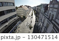 The video is an FPV First Person View drone flight down a pedestrian street in a European city. The drone flies down the street, passing by shops, restaurants, and cafes. The video is taken on a sunny 130471514