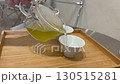 Pouring fresh green tea from glass teapot into white ceramic cup on wooden tray, symbolizing relaxation, mindfulness, Asian tea culture, healthy lifestyle, and peaceful refreshment 130515281