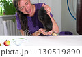 A woman plays and holds three colorful mini rabbits in her hands. She sits at a table. 130519890