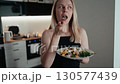 Portrait of blond woman enjoying nutrient rich salad in contemporary kitchen, savoring fresh ingredients with mindful eating. Blond woman eating vibrant salad in sleek kitchen, enjoying every bite 130577439