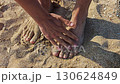 A Man brushes sand off his feet with his hands 130624849