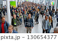 A bustling crowd attending a conference fills a large hall, moving towards exhibition booths and networking opportunities during a busy industry event. 130654377