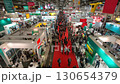 A bustling trade show floor is captured from an elevated perspective, showcasing a dynamic scene of industry networking and commercial exhibitions. 130654379