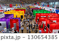 An aerial perspective captures the bustling activity of people navigating an expansive trade show filled with vibrant, colorful booths and numerous exhibitors. 130654385