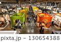 Wide-angle view of people walking through a modern trade show, featuring colorful exhibit booths, displays, and interior designs, creating a vibrant convention atmosphere. 130654388
