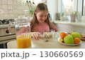 smiling girl sits at a kitchen table with a bowl of oatmeal, a pitcher of orange juice, and a plate 130660569