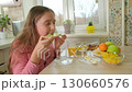 A young girl in a pink shirt takes a bite from a crispbread with cream cheese and cucumber. Healthy 130660576