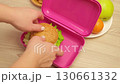 Hands of a mother putting a cheese, tomato and lettuce sandwich, fruits and cookies into a lunch box 130661332
