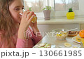 Kid girl in a pink shirt drinks a glass of orange juice. Healthy breakfast and a cheerful morning 130661985