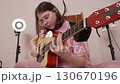 Young woman with eyes closed performs energetically on classical guitar. She uses guitar pick and strumming style to create powerful musical performance in home studio. Close-up, handheld shot Young woman with eyes closed performs energetically on classical guitar. She uses guitar pick and strumming style to create powerful musical performance in home studio. Close-up, handheld shot 130670196