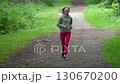 Athletic woman in sports clothing running on pathway in park during summer sports training. Female fitness model wearing green hoodie, red joggers and sports sneakers. Full length, real time Athletic woman in sports clothing running on pathway in park during summer sports training. Female fitness model wearing green hoodie, red joggers and sports sneakers. Full length, real time 130670200