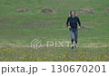 Woman runner wearing sportswear - tracksuit jacket, cropped leggings and sneakers running through field in ankle deep grass during summer sports training. Full length, front view, real time video Woman runner wearing sportswear - tracksuit jacket, cropped leggings and sneakers running through field in ankle deep grass during summer sports training. Full length, front view, real time video 130670201