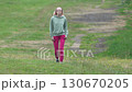 Full length view of slender woman during summer sports training walking through field in short grass. Female fit model in sportswear - light green hoodie, red joggers, sports shoe. Real time, zoom out Full length view of slender woman during summer sports training walking through field in short grass. Female fit model in sportswear - light green hoodie, red joggers, sports shoe. Real time, zoom out 130670205