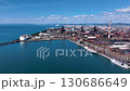Drone footage of a vast coastal industrial area with rusty remains shining against the natural light of blue sea, blue sky, and white clouds. 130686649