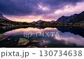 A tranquil landscape of symmetrical reflections of the alpine lake reflecting the sunset between the clouds and the sharp ridges 130734638