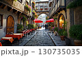 Cobblestone alleys, flowered balconies, and cafe terraces lined with red umbrellas in the old European town, with morning light and bustle 130735035