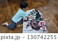 A young child engrossed in the act of painting with vivid colors. The child is sitting on the floor, fully focused on the creative process, mixing paint in a small dish. 130742255
