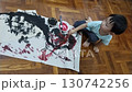 A young child engrossed in the act of painting with vivid colors. The child is sitting on the floor, fully focused on the creative process, mixing paint in a small dish. 130742256