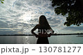 A beautiful silhouette standing gracefully by the peaceful and serene lakeside at sunset 130781277