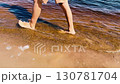 Person walking barefoot along sandy beach shoreline, with gentle waves lapping at feet, creating a serene atmosphere 130781704