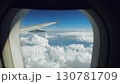 Airplane wing visible through aircraft window, showcasing a breathtaking view of fluffy white clouds and a clear blue sky 130781709