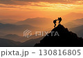Silhouette of two hikers reaching the mountain peak, symbolizing freedom and adventure in nature 130816805