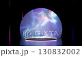 Minimalist 3D render of a glowing circular podium on a dark reflective stage, set against a vibrant, abstract semi-circular background with iridescent, flowing light patterns and neon vertical bars. 130832002