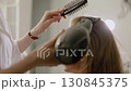Hair dryer, drying. Hair dryer blowing on attractive Caucasian woman hair, makeup artist hairdresser combing hair with comb. Close-up 130845375