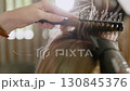 Hair dryer blows on a woman hair, which is combed with comb. Close-up 130845376