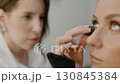 Under-eye shadow corrector, foundation. Makeup artist applies under-eye shadow corrector cream to model face and smears it with sponge. Close-up 130845384