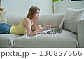 Young student girl study online, lying at home on couch with laptop, textbook 130857566