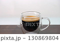 Adding whole 3 sugar cubes to hot black coffee in double wall clear glass cup 130869804