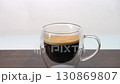 Adding whole 3 sugar cubes to hot black coffee in double wall clear glass cup 130869807