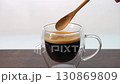 Adding 3 wooden spoons of brown sugar to hot black coffee in double wall clear glass cup 130869809