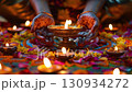 close up of woman's hands with traditional mehendi designs place a glowing diya lamp on a rangoli decorated floor surrounded by marigolds, symbolizing spiritual offering during the festive ritual. 130934272