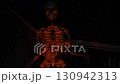Giant Halloween skeleton glows orange against a dark suburban house. Ribs, spine, pelvis, and arms are lit with dramatic light for a spooky night scene. 130942313