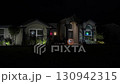 Suburban house decorated for Halloween at night with an inflatable jack-o-lantern and window lights. The porch and yard glow with festive decor in a cozy neighborhood scene. 130942315