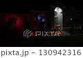 Suburban house decorated for Halloween at night with pumpkin projections, glowing lights, and spooky figures. Silhouetted trick-or-treaters walk along the path, showing costumes, candy, and family fun 130942316